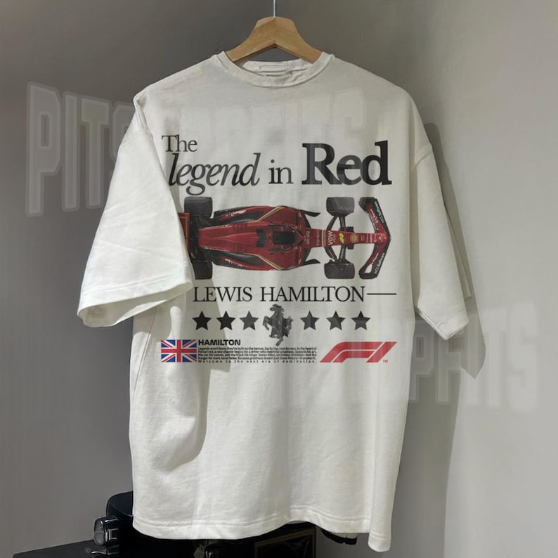 Puede incluir: Camiseta blanca con un gr&aacute;fico de coche de carreras de F&oacute;rmula 1 rojo, negro y blanco. El texto "The legend in Red" est&aacute; por encima del coche y "Lewis Hamilton" est&aacute; por debajo del coche. El texto "Hamilton" est&aacute; en una fuente m&aacute;s peque&ntilde;a y est&aacute; debajo de una bandera del Reino Unido.