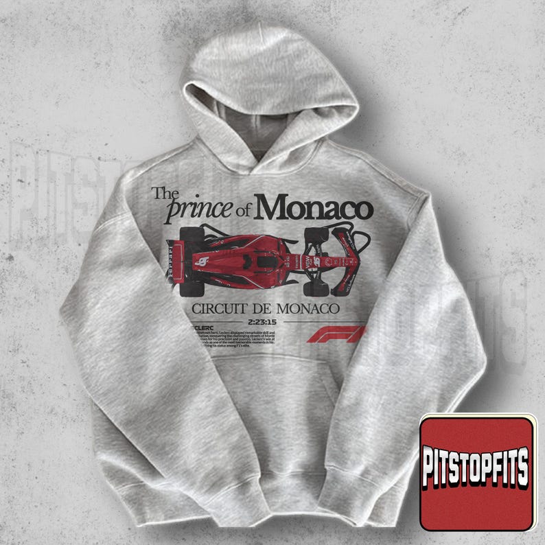 May include: A light gray hoodie with a hood and a front pocket. The front of the hoodie features a red and black graphic of a race car with the text "The Prince of Monaco" and "Circuit De Monaco".