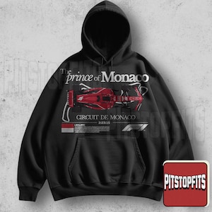 May include: Black hooded sweatshirt featuring a red race car graphic with the text "The Prince of Monaco" and "Circuit de Monaco". The design includes the F1 logo and the text "Leclerc 2-23-15".