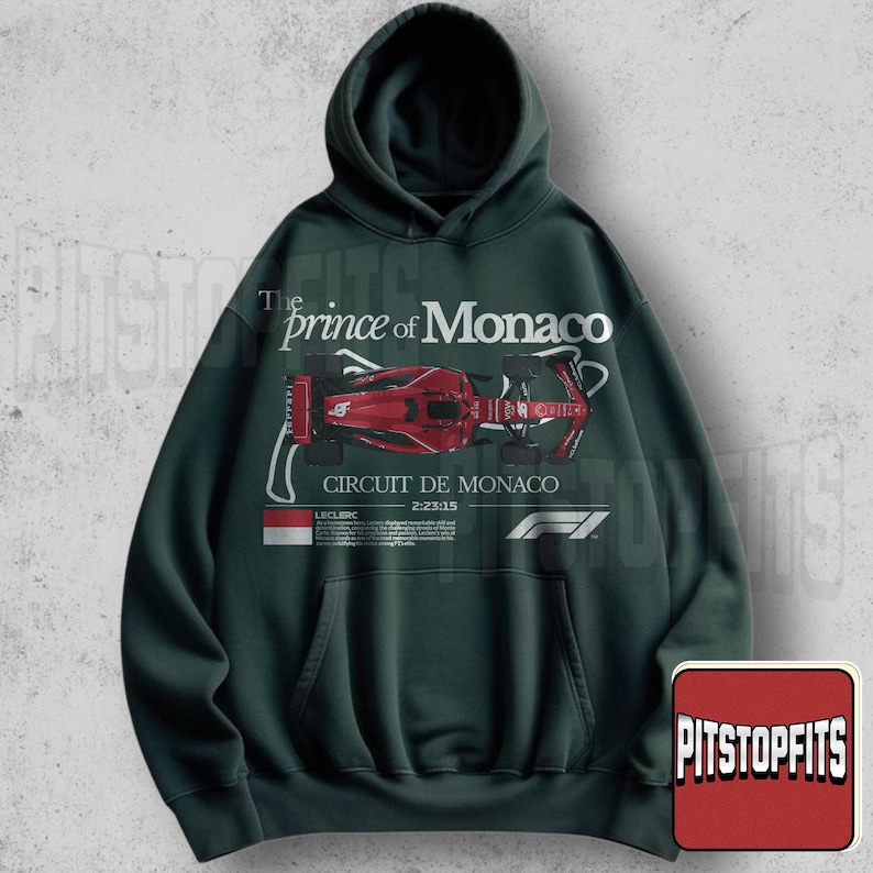 May include: Dark green hoodie with a hood and a front pocket. The front features a red race car graphic with the text "The Prince of Monaco" and "Circuit de Monaco". The F1 logo is also visible.