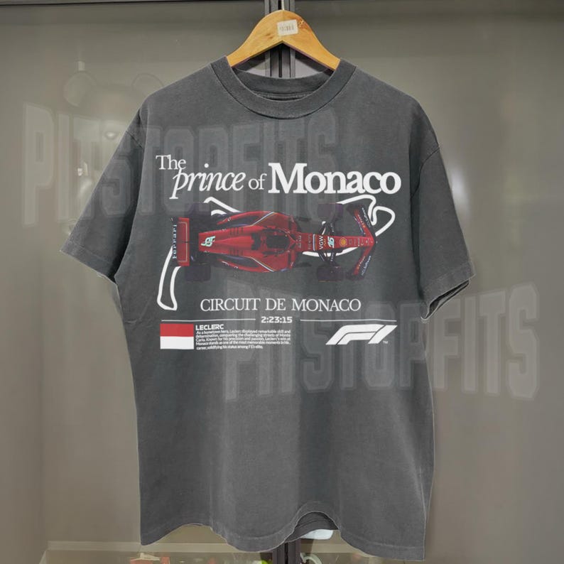May include: A dark gray t-shirt with a faded vintage look featuring a red Formula 1 race car on the front. The text "The Prince of Monaco" and "Circuit de Monaco" are printed on the shirt. The shirt also features the Formula 1 logo.