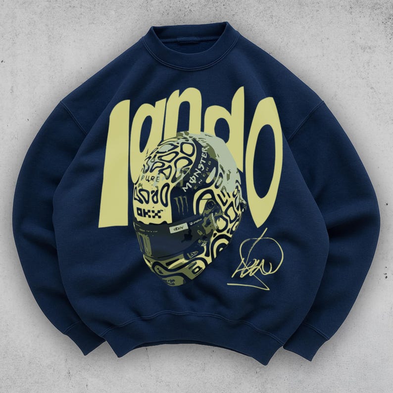 May include: Navy blue sweatshirt featuring the name "lando" in a yellow, bold font. The design includes a detailed illustration of a racing helmet with various logos and a signature. The sweatshirt is a crew neck style.