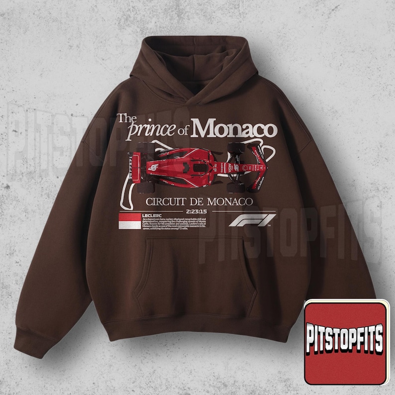 May include: Brown hoodie with a front graphic featuring a red race car and the text "The Prince of Monaco CIRCUIT DE MONACO". The hoodie has a kangaroo pocket and a drawstring hood.