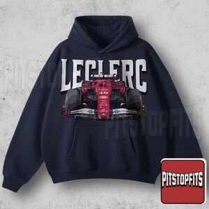May include: Navy blue hoodie featuring a red and black race car graphic with the name "LECLERC" in white block letters. The hoodie has a front pocket and a drawstring hood. The Pitstopfits logo is in the bottom right corner.
