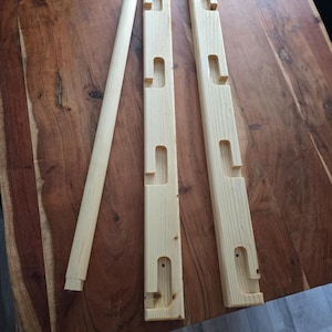 May include: Three wooden pieces for a DIY wall-mounted coat rack. Two pieces have five cut-out slots for hooks. The third piece is a long, round dowel.
