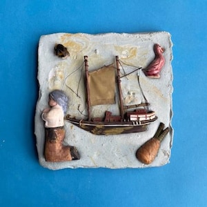Op de afbeelding: Een klein, gedetailleerd, driedimensionaal tafereel van een schip met een zeil, een knielende persoon, een vogel en een wortel op een getextureerde, grijze achtergrond.