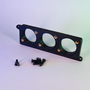 May include: A black rectangular bracket with three circular openings and several small gold-colored screws. A few additional screws are scattered nearby. The bracket has a small tab on one end.