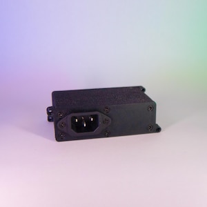 May include: A black rectangular electrical component with a three-prong power inlet. The component is secured with multiple screws and has a textured surface. The background is a gradient of purple and green.