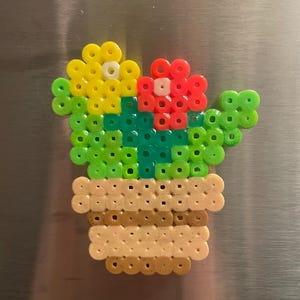 May include: A green cactus with yellow and red flowers in a brown pot. The cactus is made of small plastic beads.