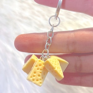 Könnte beinhalten: Ein Schlüsselanhänger mit einem Bündel aus vier kleinen, gelben, käseförmigen Anhängern, die an einer silbernen Kette befestigt sind.