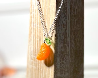 May include: A silver chain necklace with a small orange slice pendant and a green leaf charm.