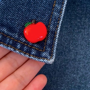 Pode incluir: Um alfinete de maçã vermelho em uma jaqueta jeans azul.