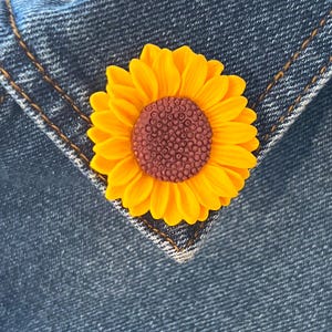 Op de afbeelding: Een gele zonnebloem met een bruin hart, vastgemaakt aan een blauwe denim stof.
