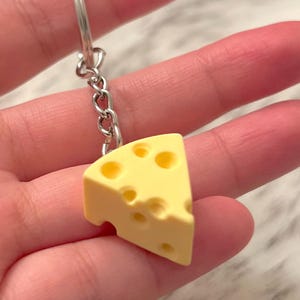 May include: A yellow cheese keychain with holes, attached to a silver chain.