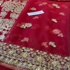 May include: A red dupatta with gold and silver embroidery. The dupatta has a delicate floral pattern and is embellished with sequins. The word "DUPATTA" is printed on a white tag. The fabric is sheer and lightweight.
