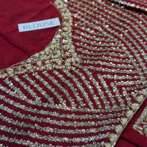 May include: A red blouse with intricate gold sequin detailing. The sequins are arranged in a striped pattern across the bodice. The word "BLOUSE" is printed on a white tag.