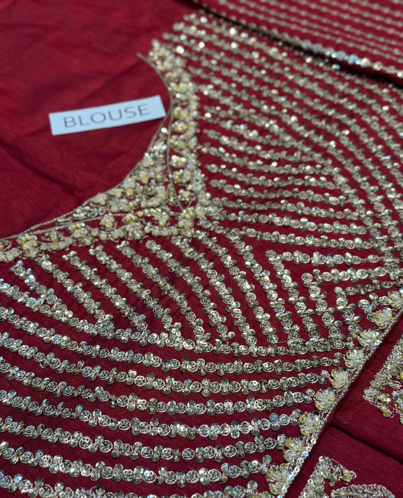 May include: A red blouse with intricate gold sequin detailing. The sequins are arranged in a striped pattern across the bodice. The word "BLOUSE" is printed on a white tag.