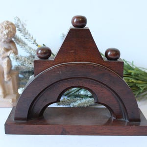 May include: A dark brown wooden arch-shaped stand featuring a flat rectangular base and three smooth spherical finials positioned along the top edge. The structure has a central arched cutout and a polished finish, showcasing the natural wood grain.
