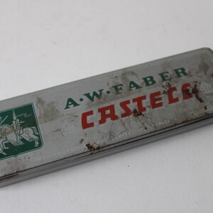 Pode incluir: Estojo de l&aacute;pis A.W. Faber Castell vintage. O estojo retangular de lata &eacute; cinza com letras verdes e vermelhas. Um emblema verde com cavaleiros a cavalo est&aacute; no lado esquerdo. O estojo mostra sinais de idade e desgaste.