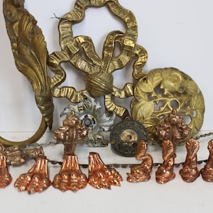 May include: A collection of antique brass and copper decorative hardware pieces. Includes ornate hooks, floral accents, and claw feet. The pieces are in various shades of gold and copper, with intricate detailing.