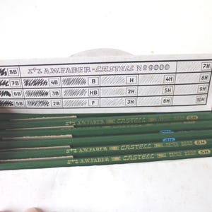Pode incluir: Uma caixa de l&aacute;pis A.W. Faber-Castell No. 9000. Os l&aacute;pis s&atilde;o verdes com letras douradas. A tampa mostra os graus de dureza da grafite do l&aacute;pis, de 8B a 10H. A caixa est&aacute; aberta, revelando os l&aacute;pis.
