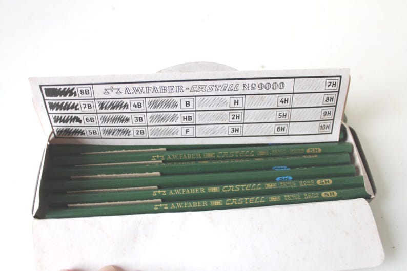 Pode incluir: Uma caixa de l&aacute;pis A.W. Faber-Castell No. 9000. Os l&aacute;pis s&atilde;o verdes com letras douradas. A tampa mostra os graus de dureza da grafite do l&aacute;pis, de 8B a 10H. A caixa est&aacute; aberta, revelando os l&aacute;pis.