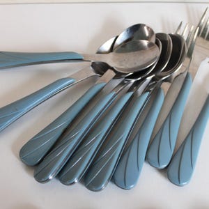 May include: A white ceramic mug with a black handle and the text "But First, Coffee" in a bold, black font. The mug is set against a blurred background, suggesting a cozy setting.