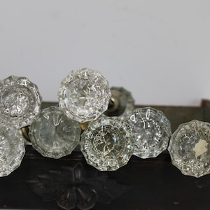 May include: A collection of six clear, faceted glass door knobs with a starburst pattern at the center. Each knob features a circular, multi-sided design with a metallic base, arranged in a cluster to display the reflective, transparent glass surfaces.
