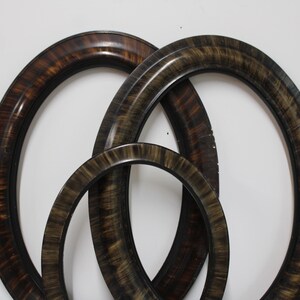 May include: Three oval-shaped picture frames with a dark brown and black faux wood grain finish. The frames are arranged in an overlapping pattern, featuring smooth, rounded edges and a glossy surface texture throughout each frame.