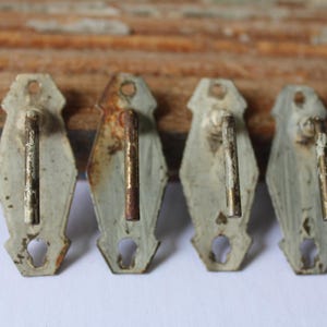 May include: Four antique metal hooks with a distressed, aged appearance. Each hook has a light green, diamond-shaped backplate with a keyhole cutout and a rusty, cylindrical hook. The hooks are arranged in a row.