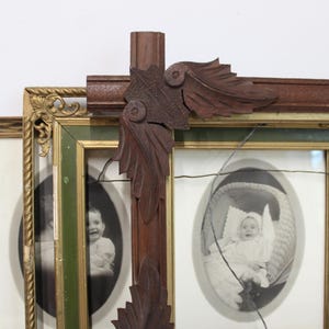 May include: A multi-paneled wooden picture frame featuring dark brown carved leaf accents at the corners. The frame contains several oval-shaped black and white photographs of infants. A thin wire runs horizontally across the front of the frame.