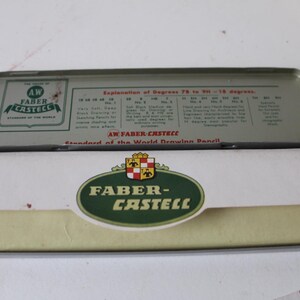 Pode incluir: Um estojo de l&aacute;pis Faber-Castell vintage aberto. A caixa de metal apresenta um logotipo verde e branco e o texto "AW FABER-CASTELL" e "Standard of the World Drawing Pencil". O estojo cont&eacute;m l&aacute;pis.