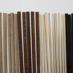 May include: A collection of long, thin, straight strips arranged vertically. The set includes several light brown wood-grain strips, dark brown wood-grain strips, metallic silver strips with tan centers, and solid black strips with a smooth finish.
