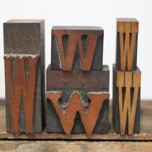 May include: A collection of five vintage wooden letterpress blocks, each featuring the letter W in varying sizes and fonts. The blocks are constructed from dark, weathered wood with the letter faces showing a lighter, natural wood grain finish.