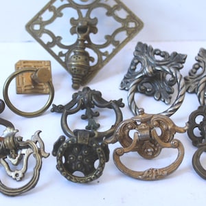 May include: A collection of antique drawer pulls and handles in various shapes and finishes. The hardware includes ornate designs in bronze, brass, and silver tones, with ring and drop pull styles. Ideal for vintage furniture restoration.