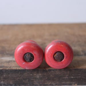 Puede incluir: Dos objetos redondos rojos con un centro oscuro y circular. Los objetos est&aacute;n colocados uno al lado del otro sobre una superficie de madera. El color rojo es uniforme y los centros oscuros contrastan.