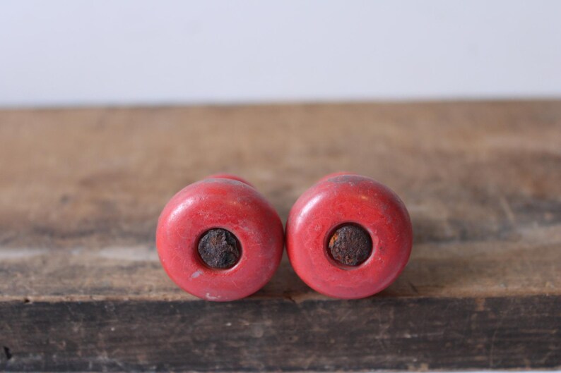 Puede incluir: Dos objetos redondos rojos con un centro oscuro y circular. Los objetos est&aacute;n colocados uno al lado del otro sobre una superficie de madera. El color rojo es uniforme y los centros oscuros contrastan.