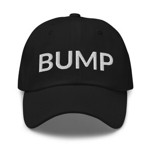 Pode incluir: Um boné de beisebol preto com a palavra "BUMP" bordada em branco na frente.