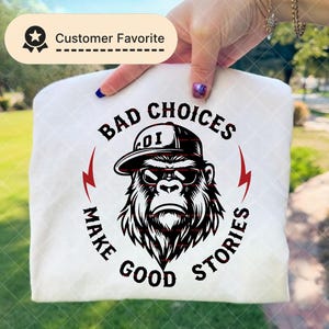 May include: White t-shirt featuring a gorilla wearing sunglasses and a cap, with the text "BAD CHOICES MAKE GOOD STORIES" in black and red. A "Customer Favorite" badge is visible.
