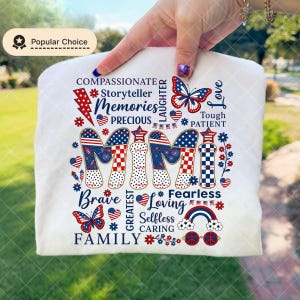May include: White t-shirt with the word "MIMI" in red, white, and blue patriotic designs. The shirt features words like "Compassionate," "Memories," and "Family," along with butterfly and star graphics. A "Popular Choice" badge is in the upper left.