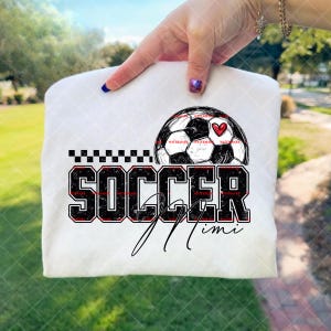 Könnte beinhalten: Weißes T-Shirt mit einer Fußballgrafik und einem roten Herz. Das Wort "SOCCER" ist in fetten schwarzen Buchstaben mit roter Umrandung geschrieben, und "Mimi" steht darunter in Schreibschrift. Ein schwarz-weißes Schachbrettmuster befindet sich über dem Wort "SOCCER".