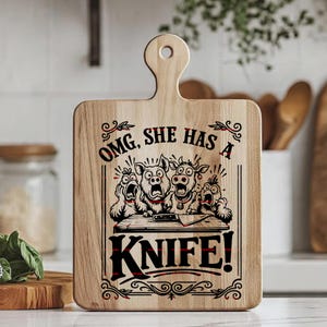 May include: A light-colored wooden cutting board with a handle featuring a black graphic print of four farm animals looking shocked behind a table with a knife. The text reads, "OMG, SHE HAS A KNIFE!" The design is framed by decorative scrollwork.