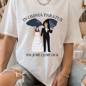 May include: White t-shirt with the text "IN OMNIA PARATUS" and "YOU JUMP, I JUMP JACK". The graphic shows a couple under umbrellas. The man is in a tuxedo, and the woman is in a wedding dress.