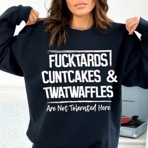 May include: A black long-sleeve crewneck sweatshirt featuring white text that reads FUCKTARDS CUNTCAKES & TWATWAFFLES Are Not Tolerated Here. The design is centered on the chest with horizontal lines above and below the main block of text.