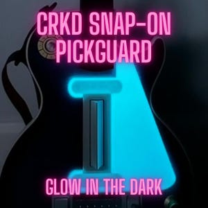 May include: A black guitar with a glowing blue pickguard. The pickguard is shaped to fit the guitar's body and has the text "CRKD SNAP-ON PICKGUARD" and "GLOW IN THE DARK" in pink neon lettering.