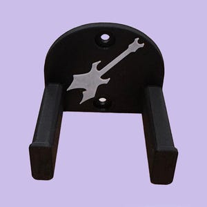 May include: Black guitar wall mount with a silver guitar-shaped accent. The mount has two arms to hold the guitar and a curved top with two holes for mounting. The guitar-shaped accent is in the center of the mount.