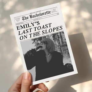 May include: A black and white newspaper-style print with the headline "Emily's Last Toast on the Slopes." The image features a person drinking from a bottle. The print is held by a hand.