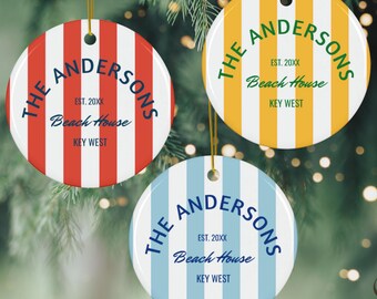 Puede incluir: Tres adornos navideños redondos con rayas verticales rojas, amarillas y azules. Cada adorno tiene el texto "THE ANDERSONS" arqueado en la parte superior, con "EST. 20XX Beach House KEY WEST" debajo. Cuelgan de cuerdas doradas.