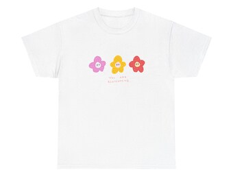 Può includere: Maglietta bianca con tre fiori colorati e il testo "You are blossoming."