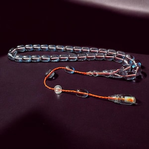 May include: A light blue glass prayer beads or rosary with a red string tassel. The beads are round and have a translucent appearance.